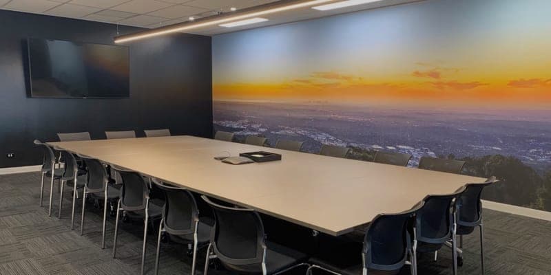 Large 25-capacity conference room with a black feature wall, wall-mounted display, and sunset landscape mural.