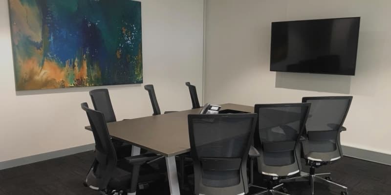 Modern 8-person meeting room with ergonomic chairs, a wall-mounted TV, and abstract art.